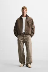 Pantalón color marrón con efecto lavado, corte relaxed fit, cinco bolsillos, aplicación de tira y bolsillo multifunción en perneras, cierre frontal con cremallera y botón.