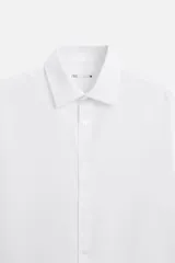 Camisa blanca de corte regular, cuello italiano, manga larga con puños abotonados y cierre frontal con botones.