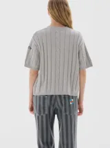 Remera de punto negra con cuello redondo y mangas cortas. Presenta un diseño de tejido con trenzas verticales.