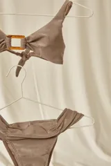 Bikini de dos piezas con top de triángulos fijos unidos por una argolla y bottom vedetina ancha, con detalles fruncidos.