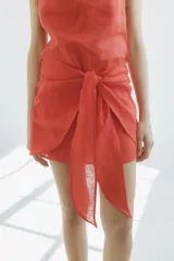 Minifalda color naranja confeccionada en lino, con corte irregular y lazo frontal para atar.
