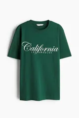 Remera verde oscuro de corte holgado en punto de algodón, con cuello redondo y estampado frontal con la palabra "California" en cursiva y "Los Angeles" debajo.