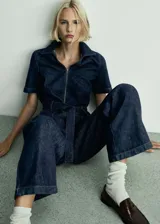 Mono largo de denim azul oscuro, con cuello camisero, mangas cortas y cierre frontal con cremallera. Incluye cinturón ajustable, bolsillos laterales y trabillas.