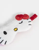 Antifaz de peluche blanco con la forma de la cara de Hello Kitty, con detalles bordados en negro y amarillo, moño rojo y elástico trasero.