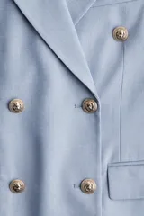 Blazer celeste de doble botonadura con solapas de pico, hombreras finas, bolsillos delanteros ribeteados con solapa y puños abotonados con abertura decorativa. Forrado.