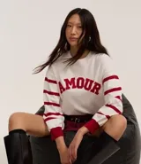 Suéter blanco de jacquard con letras 'Amour' en rojo y rayas horizontales rojas en las mangas.