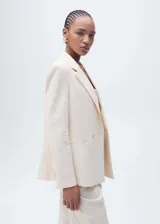 Blazer color crema con cuello de solapa, cierre cruzado con doble botonadura y corte recto.