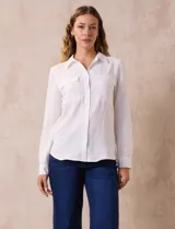 Camisa blanca de manga larga con cuello con solapa y abertura central con botones. Tiene dos bolsillos delanteros aplicados.