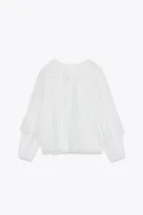 Blusa blanca semitransparente de escote pico y manga larga con puño elástico. Detalle de volantes y bordados a tono. Cierre frontal con botones.