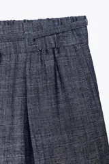 Pantalón ancho azul con textura de lino, tiro alto, cintura elástica con cordón ajustable, pinzas delanteras, bolsillos laterales y traseros, y cinturón de la misma tela con apliques metálicos.