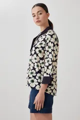 Blusa con estampa de margaritas blancas y verdes sobre fondo azul marino, con cuello polo y mangas 3/4 con puños en contraste.