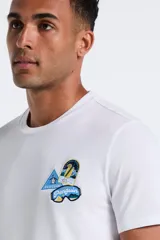 Remera blanca de manga corta con cuello redondo y un conjunto de parches bordados en el pecho izquierdo.