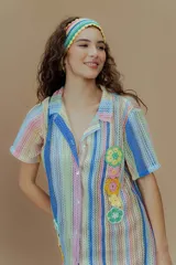 Vestido corto tejido a rayas verticales de colores pastel, con cuello camisero, cierre frontal con botones y bordado de flores de crochet.