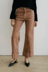 Pantalón de jean azul oscuro con corte acampanado, tiro medio y dobladillo en el ruedo. Presenta costuras marcadas en el frente y estampado abstracto en tonos grises y blancos en el interior del dobladillo.