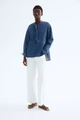 Blusa azul de denim con cuello redondo, tapeta con botones ocultos y mangas largas con puños abotonados.