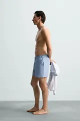 Short de baño celeste de tejido técnico con cintura elástica ajustable con cordón interior y trabillas laterales. Tiene bolsillos frontales y bolsillo trasero con cierre de cremallera. Cuenta con forro interior y cierre frontal con cremallera y botón a presión oculto.