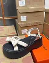 Sandalias con plataforma color negro, con tira delantera ancha color crema con detalle de moño y tira trasera con hebilla.