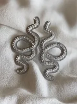 Par de aros colgantes con forma de serpiente dorada contorneada con strass. Cierre a presión de acero inoxidable.