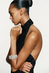 Top negro con cuello halter drapeado ajustable con botones y hombros descubiertos. Detalle de aplicación de strass combinado a tono. Forro interior y cierre en espalda con cremallera.