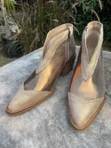 Botín de cuero color dorado con puntera y talón en gamuza color beige. Tiene cierre lateral y taco de madera.