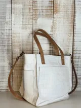 Cartera tipo tote color blanco con textura tipo piel de cocodrilo, doble asa de mano color marrón y correa larga regulable.