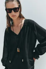 Blusa negra semitransparente con escote en pico, cordón ajustable y mangas largas con elástico en los puños.