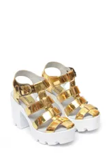 Sandalia de cuero charol con plataforma alta y hebillas, diseño elegante en color dorado y blanco.