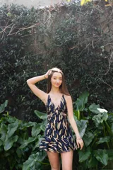 Vestido corto negro con estampado de hojas doradas, escote en V, breteles finos, argolla en el busto y cut-outs en la cintura. Falda corta con volados.