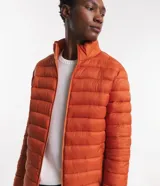 Campera puffer ultraligera color beige, con cuello alto, cierre por cremallera y bolsillos con cremallera. Incluye bolso de almacenamiento.