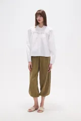 Camisa blanca de algodón con mangas largas abullonadas y cuello mao con volado. Presenta un canesú con detalles de encaje calado en el frente.