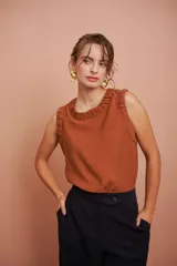 Blusa color ladrillo sin mangas con escote redondo y volados en los hombros.