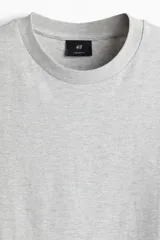 Remera de algodón pesado color gris melange, con cuello redondo ribeteado, hombros caídos y corte oversized.