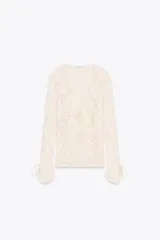 Blusa color crema de encaje con escote en V, volados y mangas largas con lazos en los puños.