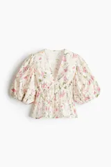 Blusa corta color blanco con estampado floral en tonos rosados y verdes. Presenta escote en V pronunciado, elásticos finos en la cintura y mangas globo cortas con elástico en los puños.