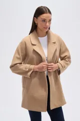 Tapado de poliéster color beige, con cuello de solapa, manga larga y cierre frontal con botones. Presenta un diseño de largo medio y detalle de botones en los puños.