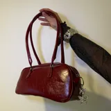 Bolso tipo baguette negro de cuero sintético con doble asa corta y cierre superior con cremallera.