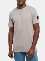 Remera gris de algodón con cuello redondo y manga corta. Presenta una insignia con el monograma de Calvin Klein en la manga izquierda.