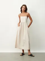 Vestido midi de color naranja, con escote recto y tirantes finos que se anudan sobre los hombros. Posee una cintura entallada con frunces que dan paso a una falda fluida.