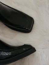 Bota de charol negra con punta cuadrada, tacón grueso y cierre lateral.