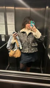 Chaqueta corta gris con estampado de rosas negras, cuello y puños de piel sintética blanca, cierre frontal con cremallera y bolsillos delanteros con solapa.