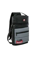 Mochila cilíndrica tipo matera, con dos compartimentos separados por cierre. El cuerpo superior es de material liso color camel y el inferior es acolchado color beige. Presenta parches circulares con motivos de naturaleza y una etiqueta verde con el texto "EXPLORE YOUR WORLD: Discovery".