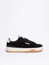 Zapatillas Tommy Jeans de corte bajo, color negro, con exterior de ante, interior de poliéster y suela de goma color caramelo. Presentan un panel a contraste en el talón, logo de Tommy Jeans en la lengüeta y etiqueta de la marca en el lateral.