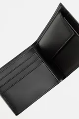 Billetera de cuero negra con costuras al tono. Cuenta con compartimento para billetes, tres compartimentos para tarjetas y un monedero con cierre mediante clip.