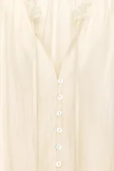 Camisa color crema de algodón con cuello redondo, escote pico con lazadas, manga larga con puños y cierre frontal con botones.
