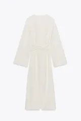 Vestido midi color crudo, con escote en V y mangas largas acampanadas. Cintura ajustable con lazos del mismo tejido.