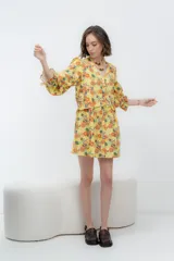 Vestido corto de lino color amarillo con estampado de flores en tonos naranjas y verdes, con mangas largas y escote en V.