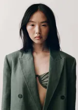 Blazer verde musgo de lino, con solapas de muesca, cierre cruzado con doble botonadura, mangas largas con puños abotonados, diseño recto, forro interior y dos bolsillos de solapa frontales.
