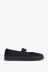 Zapato plano tipo bailarina en tejido color negro. Detalle de pespunte en el cuerpo, tira con adhesivo ajustable, suela engomada y acabado en punta redonda.