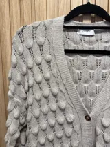 Saco de punto color gris claro con diseño de gotas en relieve, cuello en V y cierre con un botón.