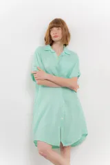 Vestido camisero corto color verde oliva, confeccionado en lino 100%. Tiene botones en la parte delantera, cuello camisero, mangas cortas con botón para arremangar y bolsillos laterales.